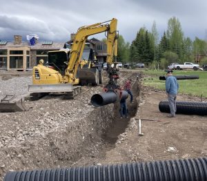 Underground utility installation in Alpine WY with excavator placing large drainage pipe in trench